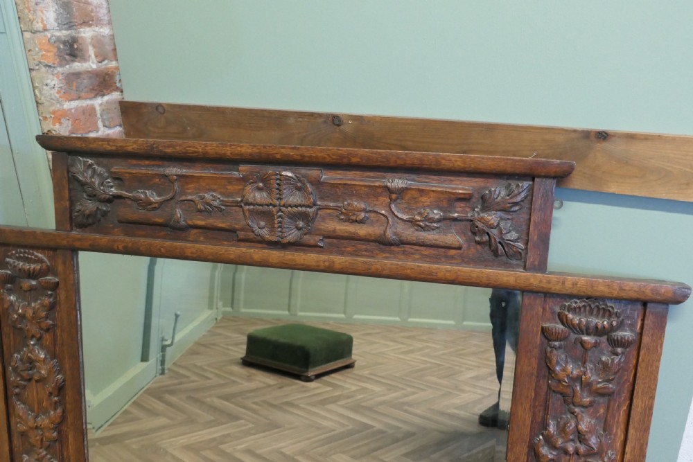 A large Arts and Crafts oak overmantel mirror featuring detailed relief carvings of thistles and stylized leaves around a rectangular glass mirror. View III