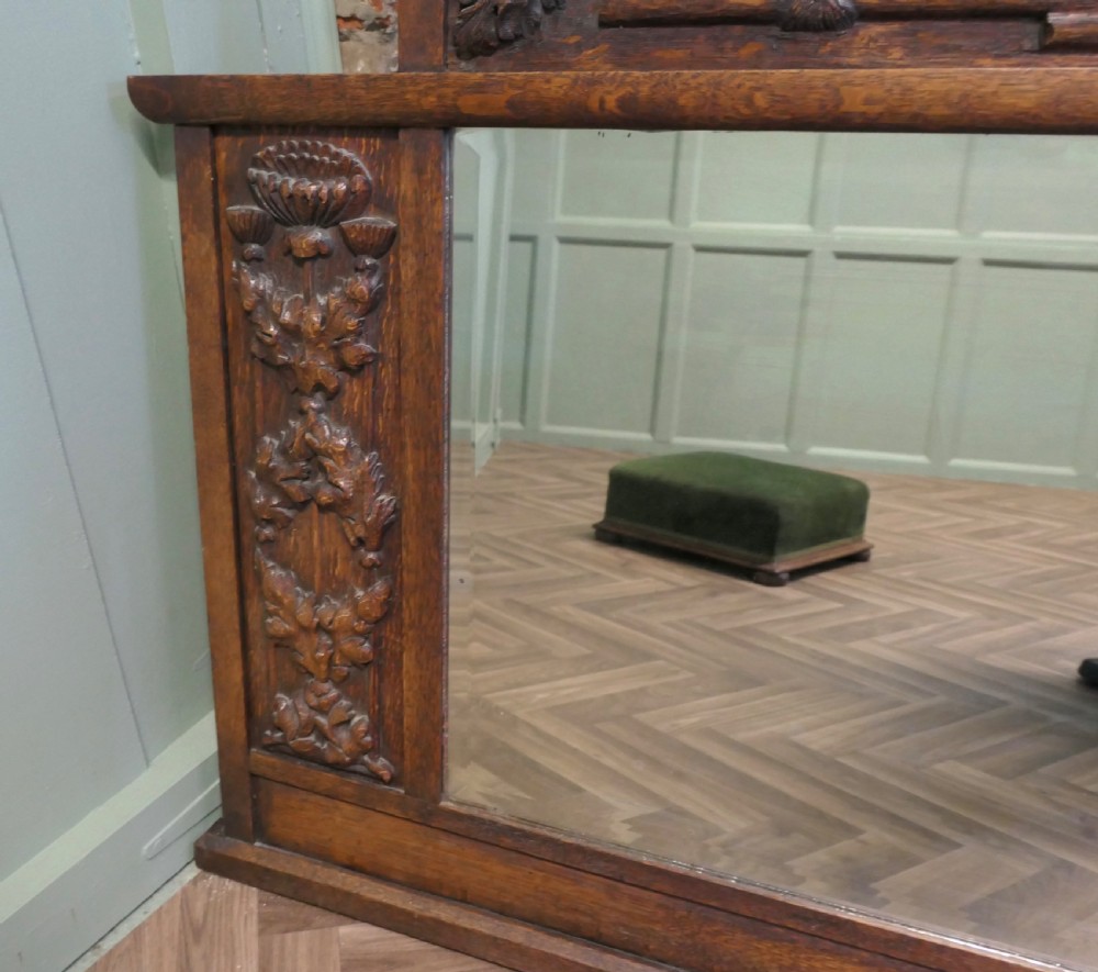 A large Arts and Crafts oak overmantel mirror featuring detailed relief carvings of thistles and stylized leaves around a rectangular glass mirror. View IV