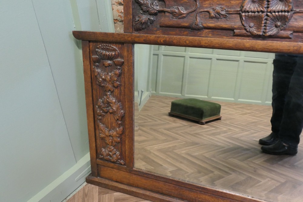 A large Arts and Crafts oak overmantel mirror featuring detailed relief carvings of thistles and stylized leaves around a rectangular glass mirror. View V