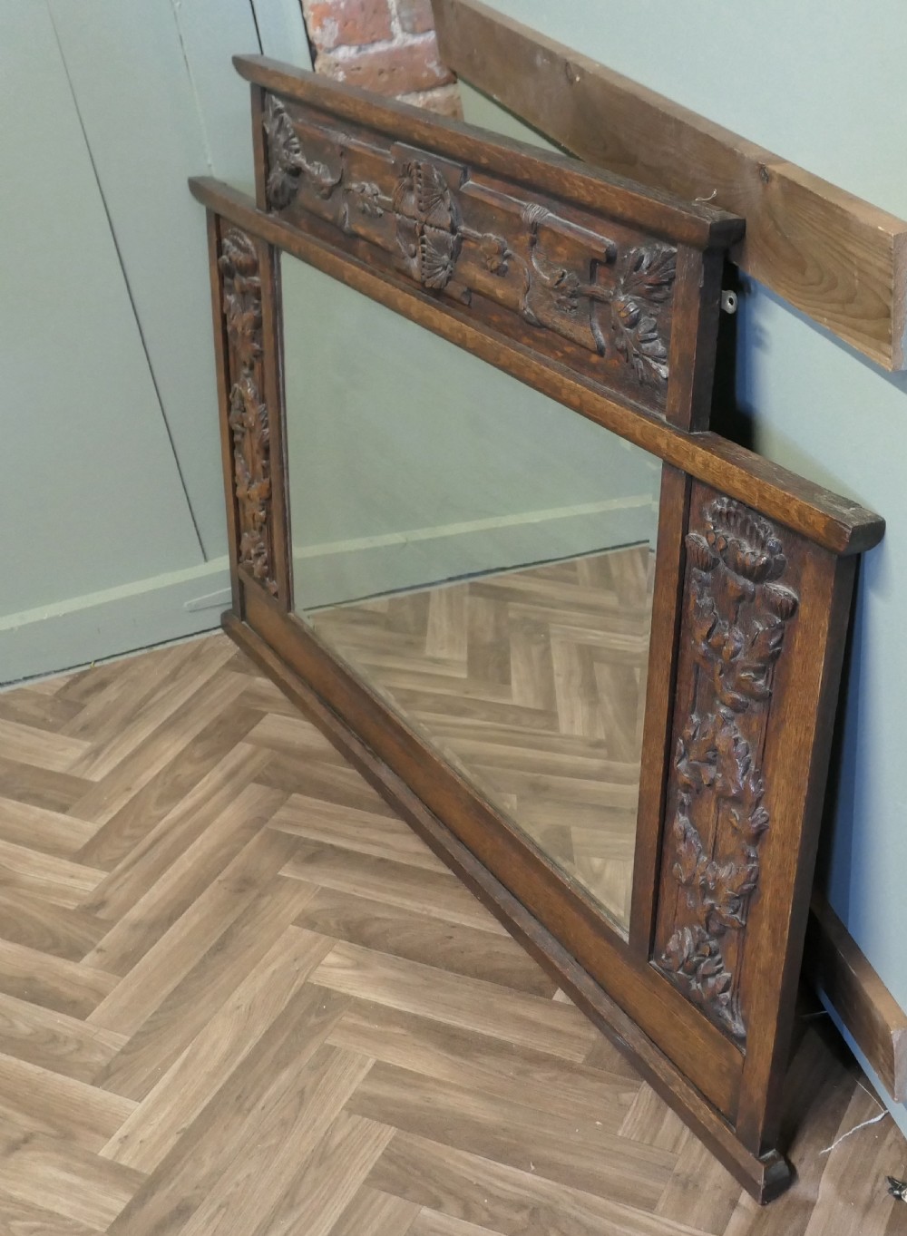 A large Arts and Crafts oak overmantel mirror featuring detailed relief carvings of thistles and stylized leaves around a rectangular glass mirror. View VI