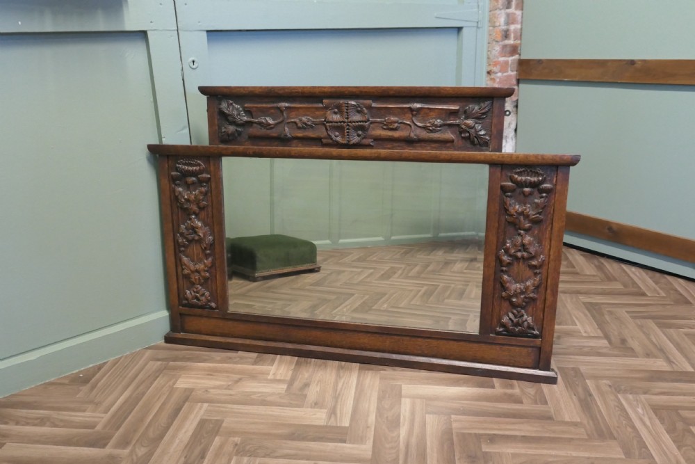 A large Arts and Crafts oak overmantel mirror featuring detailed relief carvings of thistles and stylized leaves around a rectangular glass mirror. View VII