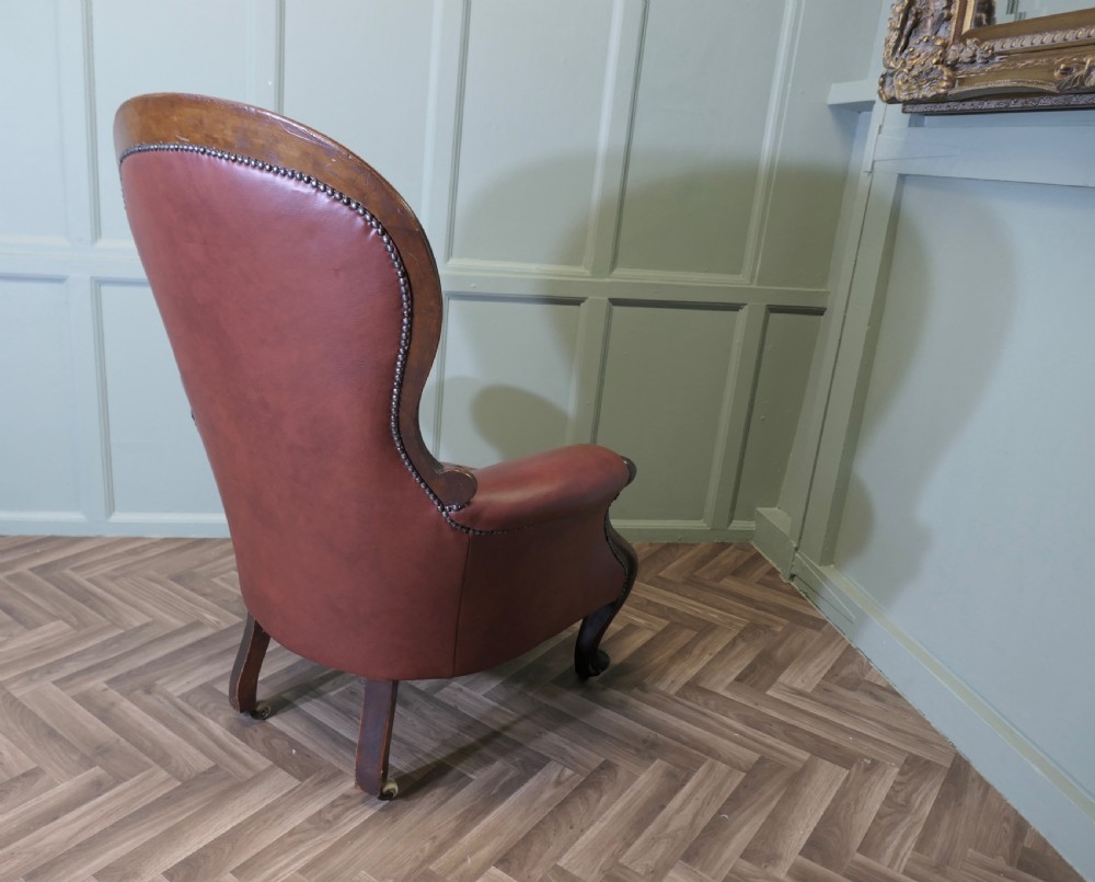 Victorian button-back salon armchair upholstered in burgundy leather with a carved dark wood frame and brass castors. View III