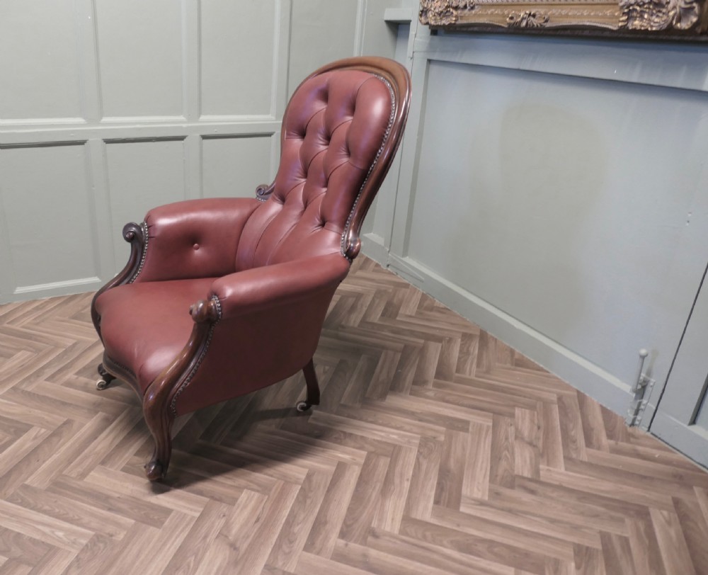 Victorian button-back salon armchair upholstered in burgundy leather with a carved dark wood frame and brass castors. View IV