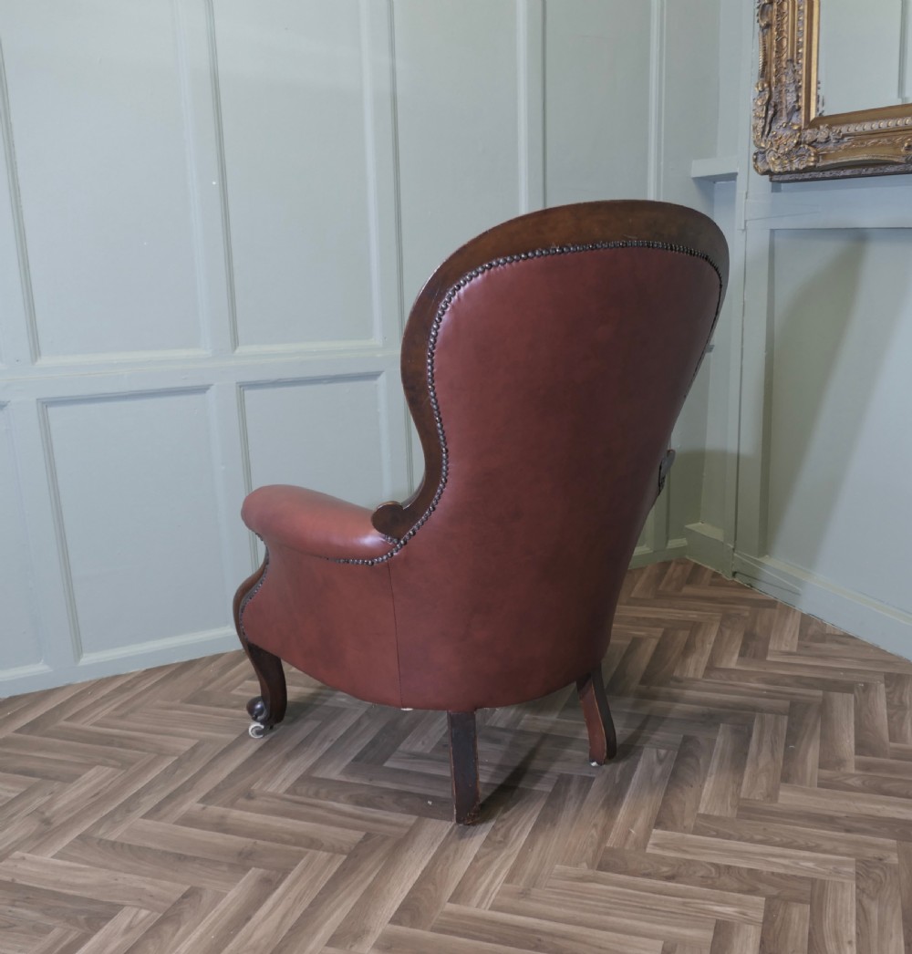 Victorian button-back salon armchair upholstered in burgundy leather with a carved dark wood frame and brass castors. View V
