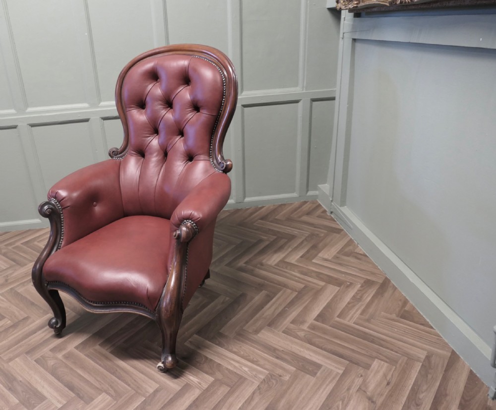 Victorian button-back salon armchair upholstered in burgundy leather with a carved dark wood frame and brass castors. View VI