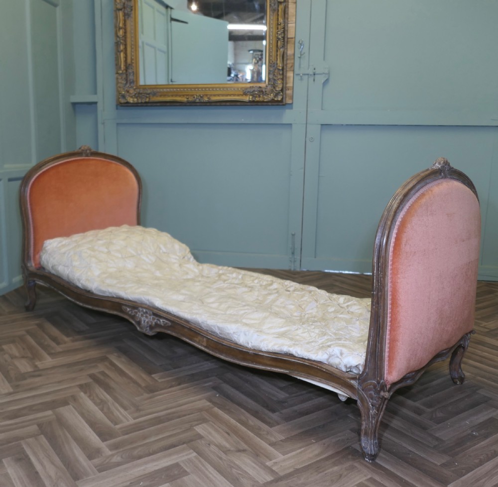 A 19th-century French carved wood daybed featuring raised terracotta velvet upholstered end panels and a tufted cream mattress cushion.