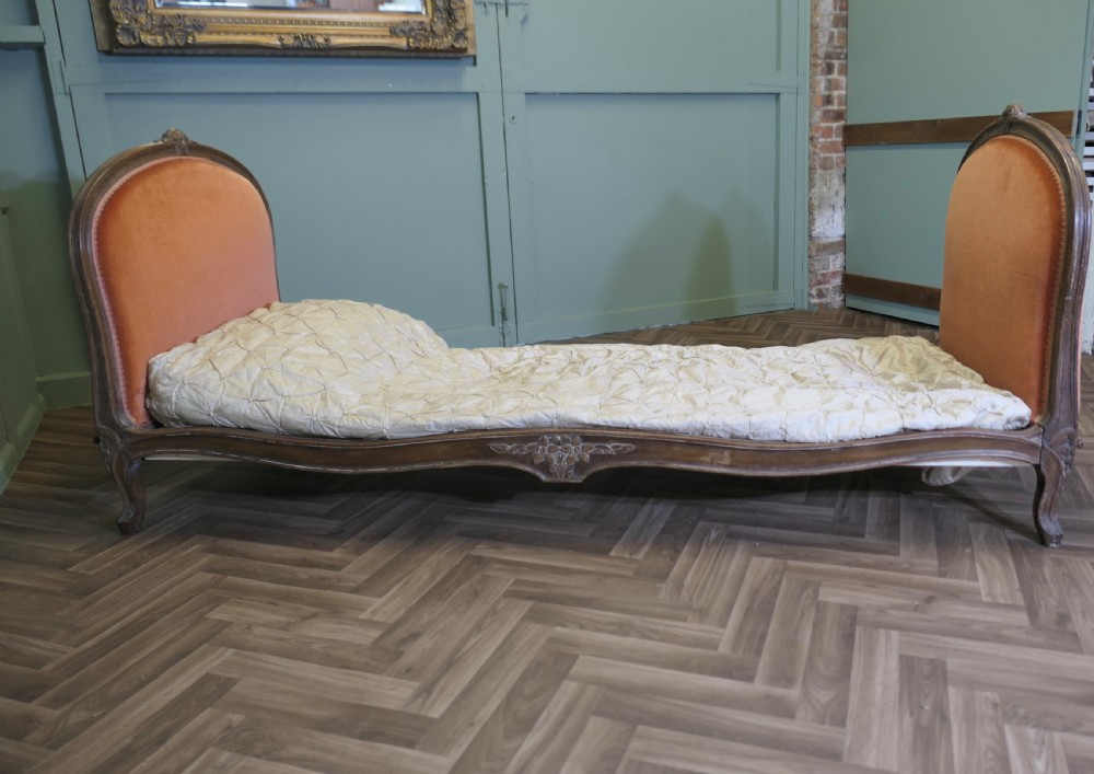 A 19th-century French carved wood daybed featuring raised terracotta velvet upholstered end panels and a tufted cream mattress cushion. View V