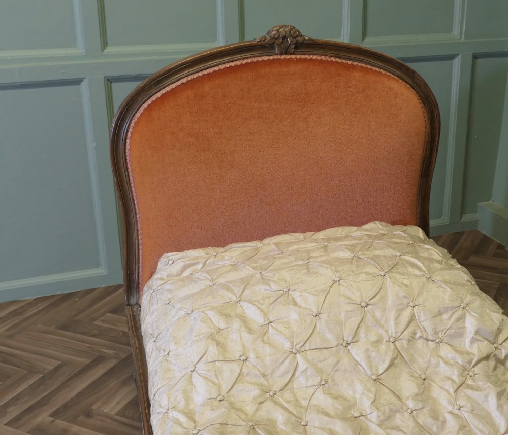 A 19th-century French carved wood daybed featuring raised terracotta velvet upholstered end panels and a tufted cream mattress cushion. View VI
