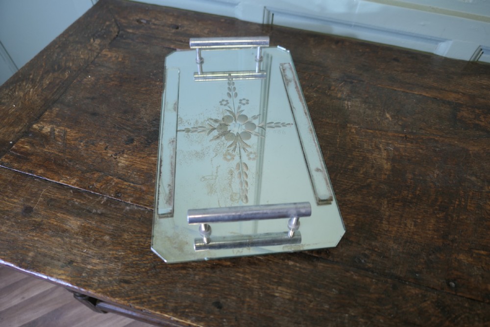 A rectangular Art Deco mirrored tray featuring central etched floral details, cut corners, and tubular silver-tone handles.