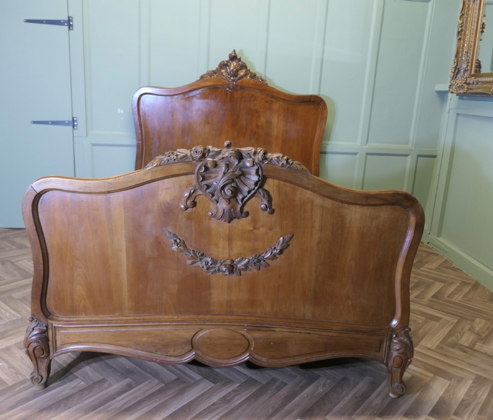 A Louis XV style carved golden walnut bed frame featuring arched headboard and footboard panels decorated with central rocaille motifs and cabriole feet.