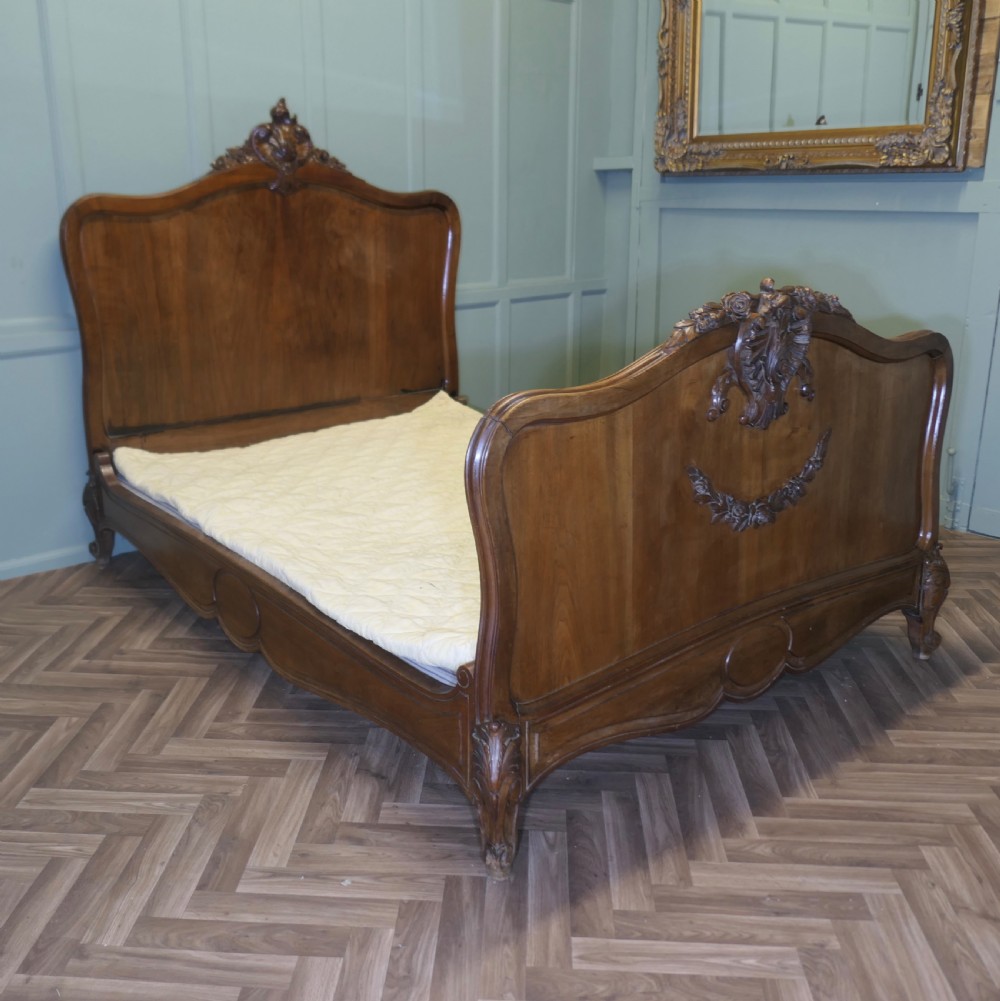 A Louis XV style carved golden walnut bed frame featuring arched headboard and footboard panels decorated with central rocaille motifs and cabriole feet. View II