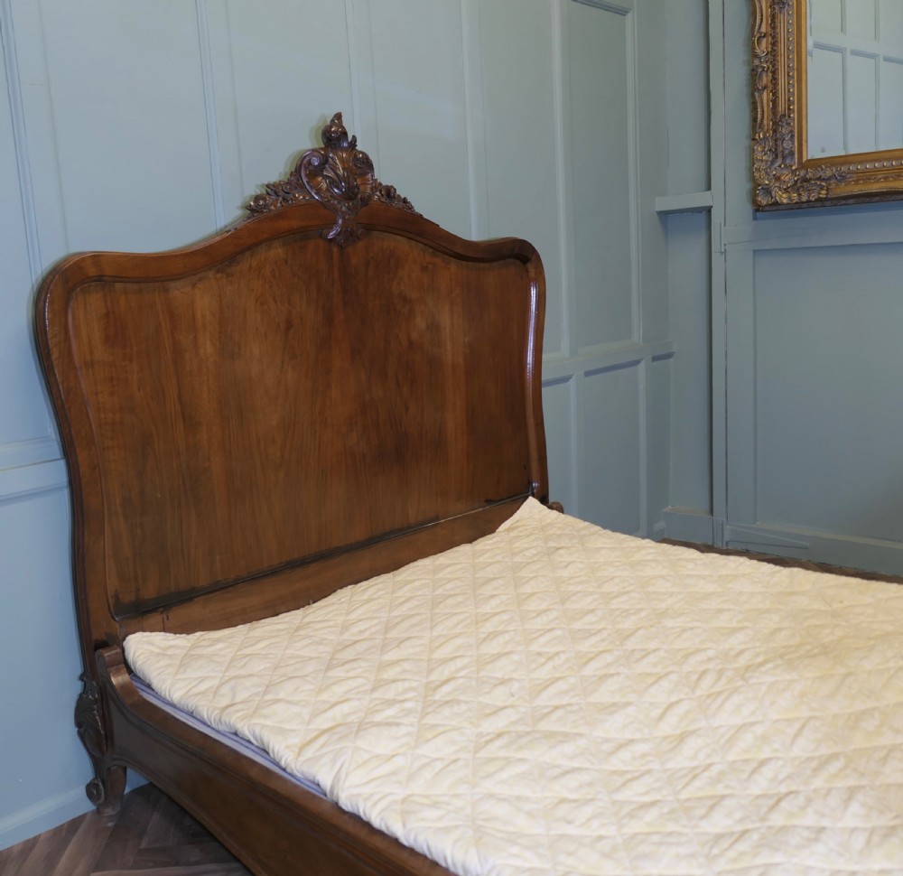 A Louis XV style carved golden walnut bed frame featuring arched headboard and footboard panels decorated with central rocaille motifs and cabriole feet. View V