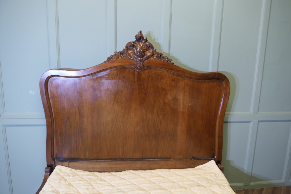 A Louis XV style carved golden walnut bed frame featuring arched headboard and footboard panels decorated with central rocaille motifs and cabriole feet. View VI