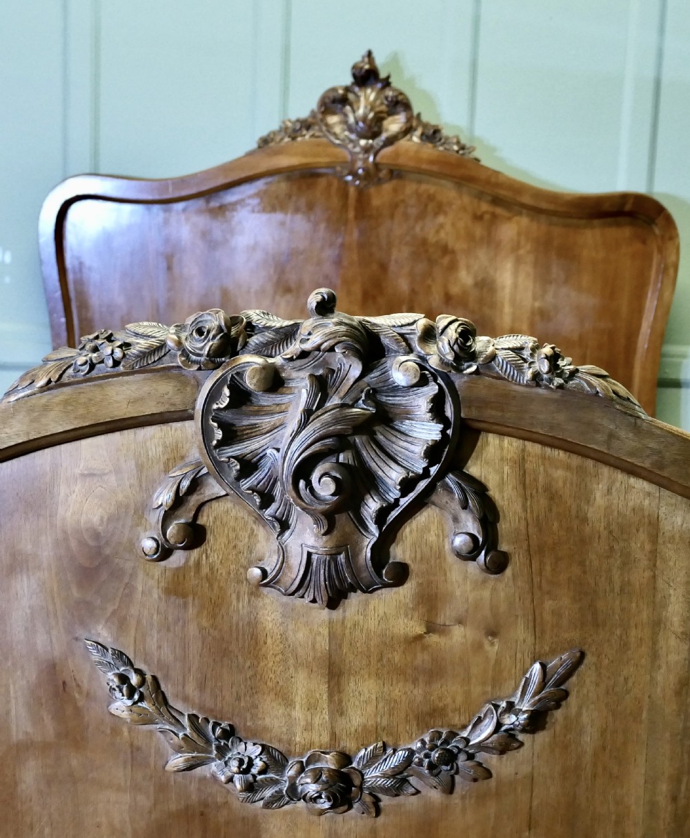 A Louis XV style carved golden walnut bed frame featuring arched headboard and footboard panels decorated with central rocaille motifs and cabriole feet. View VII