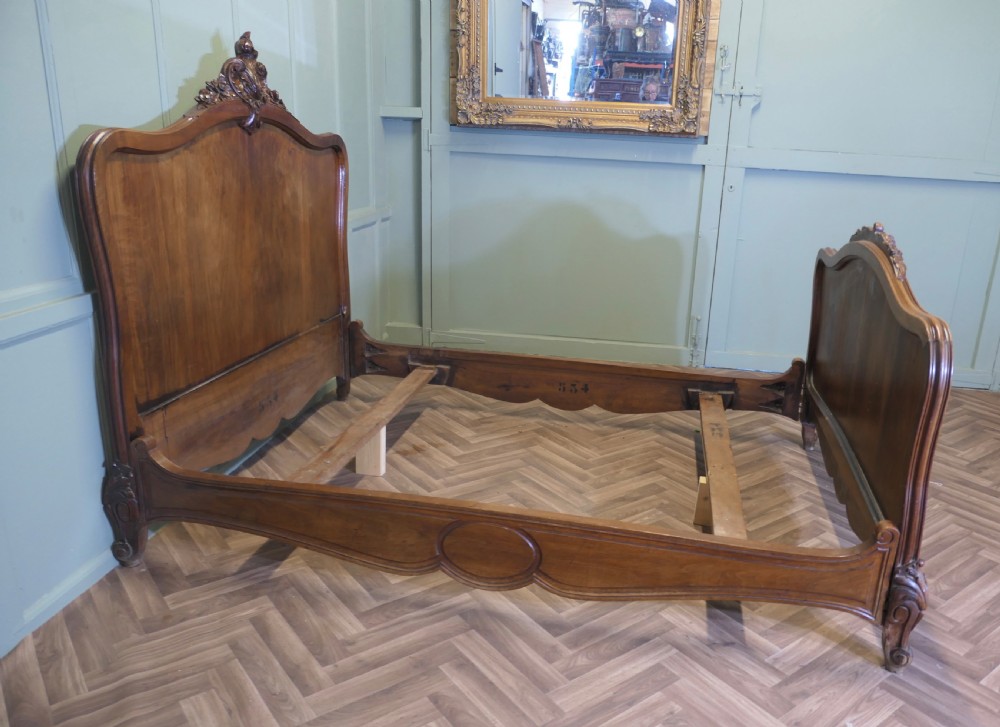 A Louis XV style carved golden walnut bed frame featuring arched headboard and footboard panels decorated with central rocaille motifs and cabriole feet. View VIII