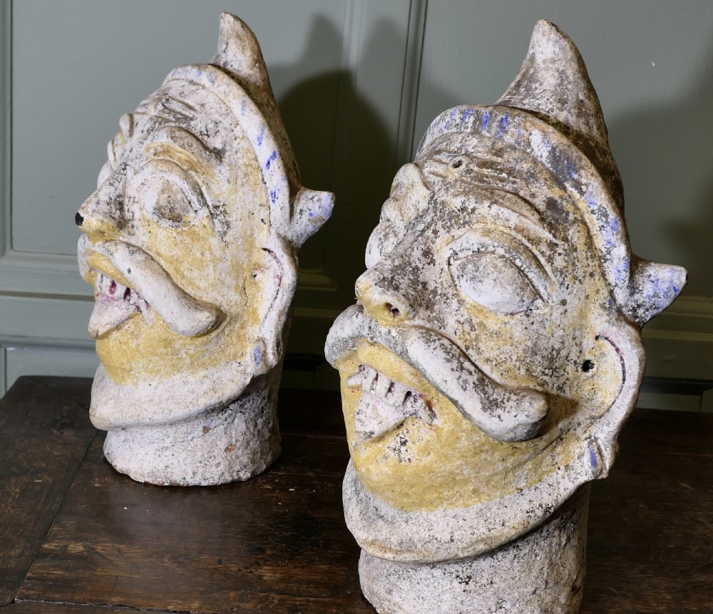 Pair of sculpted Indian terracotta tent pole tops depicting styled heads with moustaches, pointed helmets, and weathered polychrome paint. View III
