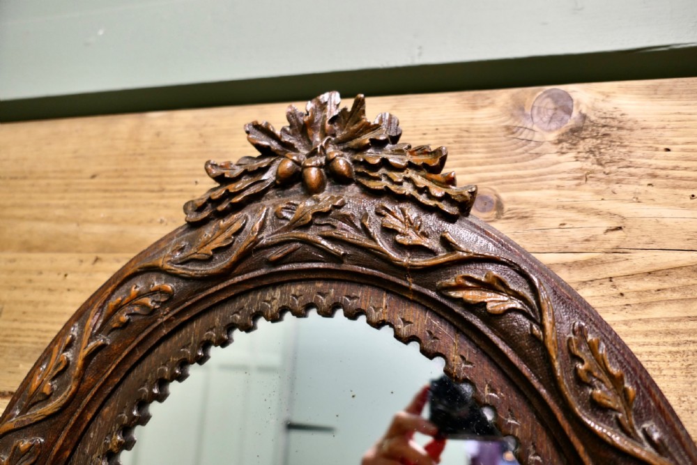 An oval dark oak wall mirror with hand-carved leaf motifs, an acorn crest top, and a notched inner border. View III
