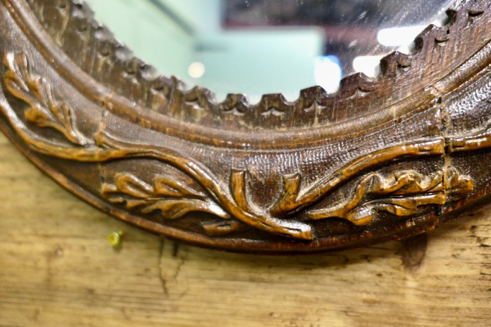 An oval dark oak wall mirror with hand-carved leaf motifs, an acorn crest top, and a notched inner border. View IV