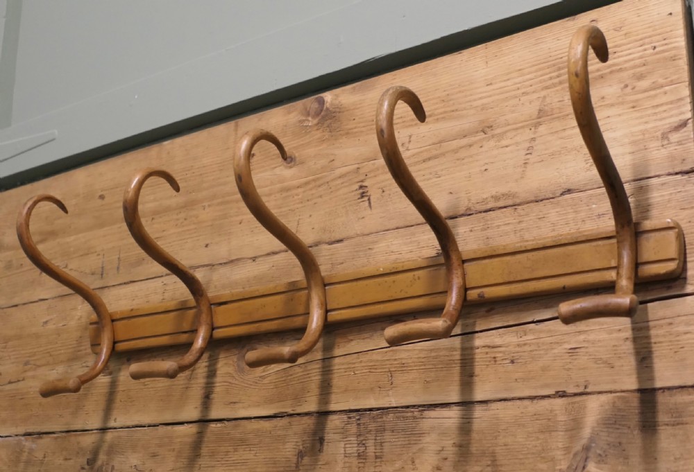 A horizontal wooden backboard holding a row of five steam-bent double hat and coat hooks.