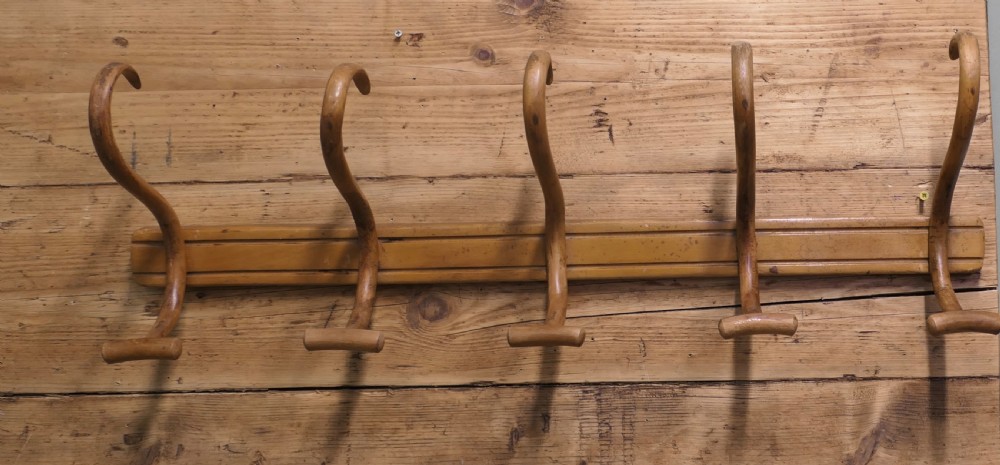 A horizontal wooden backboard holding a row of five steam-bent double hat and coat hooks. View III