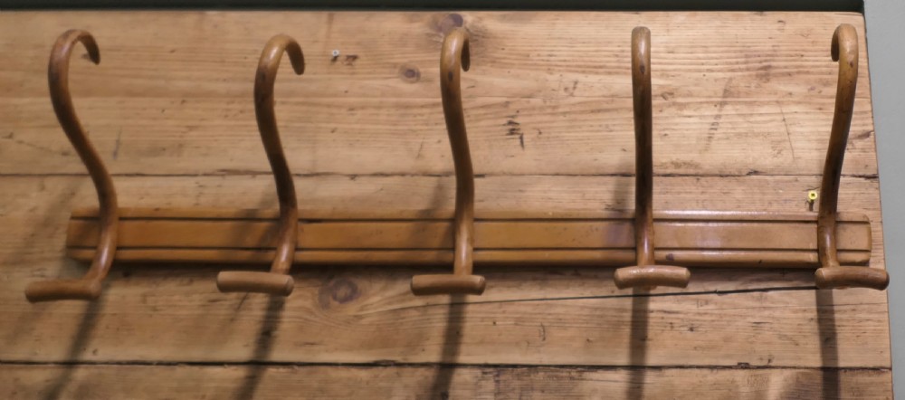 A horizontal wooden backboard holding a row of five steam-bent double hat and coat hooks. View V
