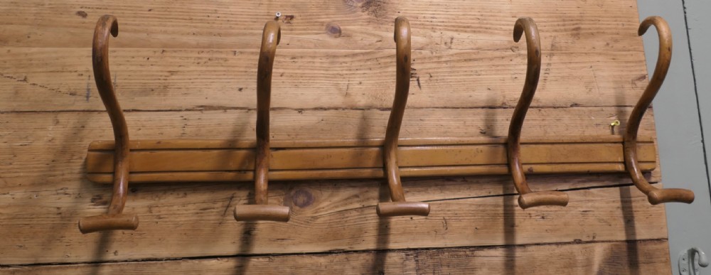 A horizontal wooden backboard holding a row of five steam-bent double hat and coat hooks. View VI