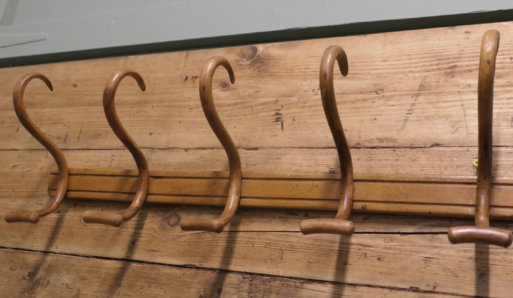 A horizontal wooden backboard holding a row of five steam-bent double hat and coat hooks. View VII