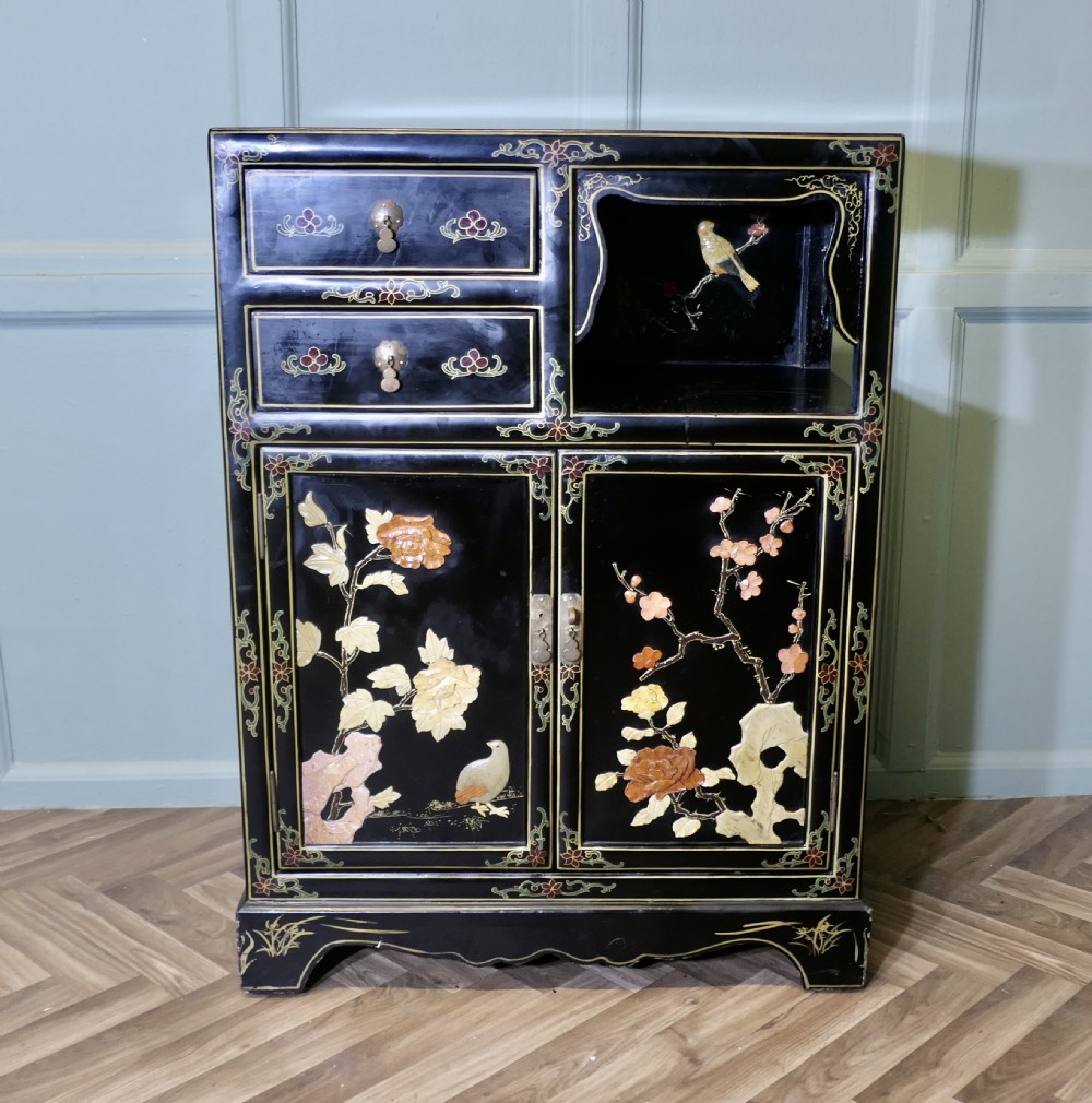 A black lacquered Chinoiserie cupboard featuring two drawers, an open upper display niche, and lower double doors decorated with floral and bird inlays.