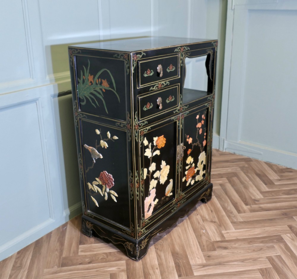 A black lacquered Chinoiserie cupboard featuring two drawers, an open upper display niche, and lower double doors decorated with floral and bird inlays. View V