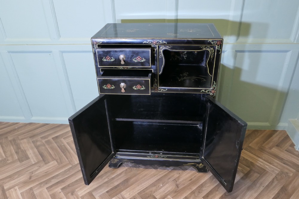 A black lacquered Chinoiserie cupboard featuring two drawers, an open upper display niche, and lower double doors decorated with floral and bird inlays. View VI
