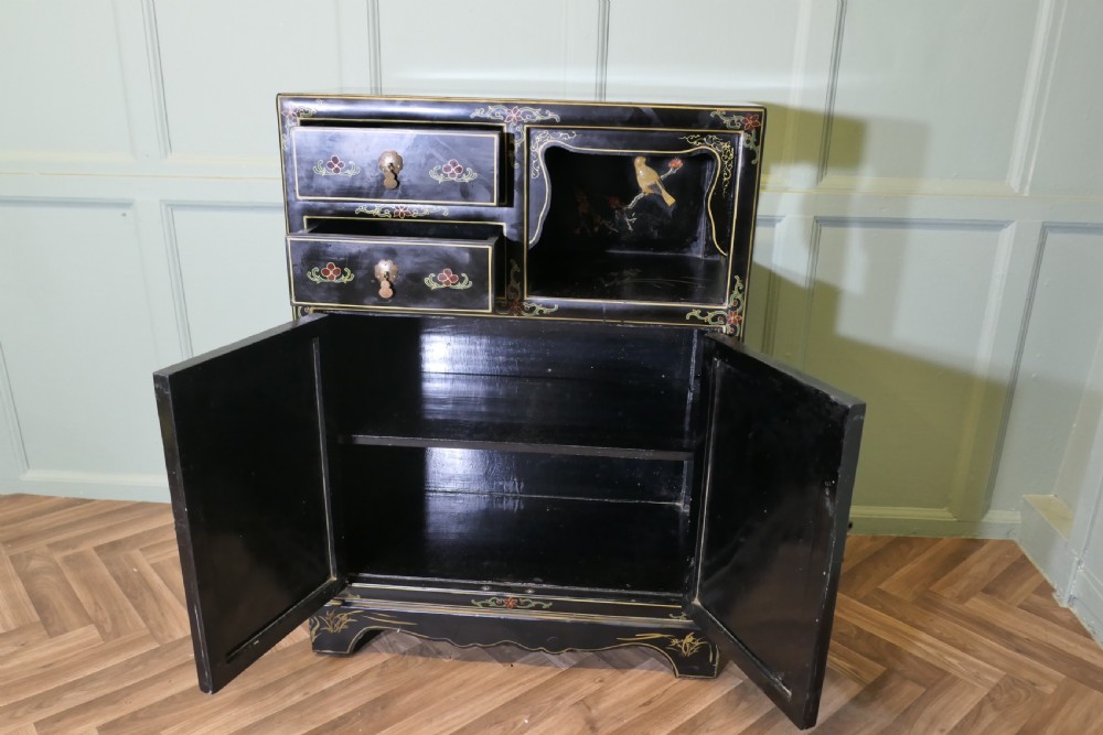 A black lacquered Chinoiserie cupboard featuring two drawers, an open upper display niche, and lower double doors decorated with floral and bird inlays. View VII