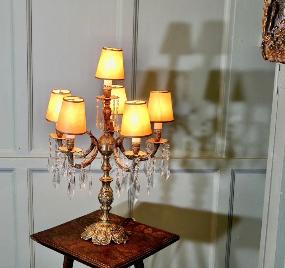 An ornate French brass six-arm girandole table lamp featuring hanging crystal prisms and small cream lampshades. View II