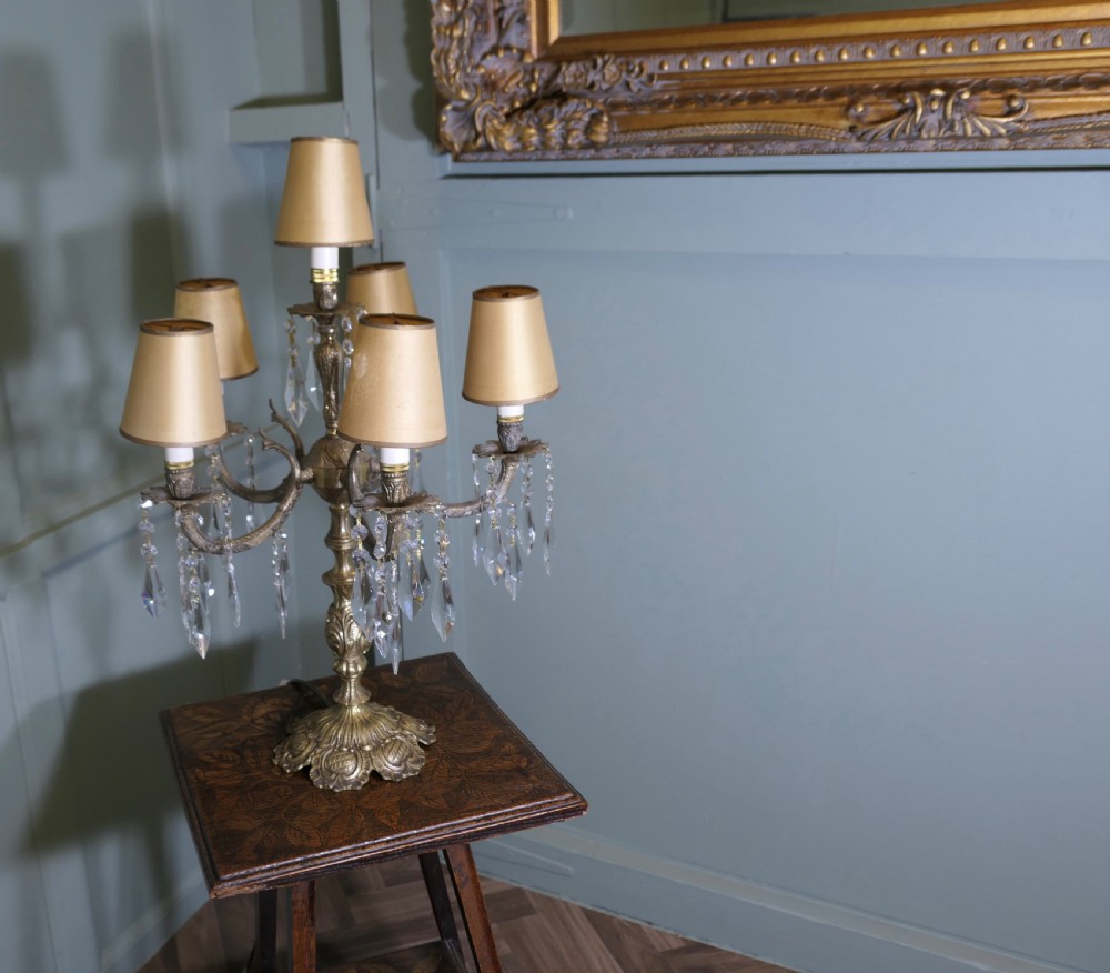 An ornate French brass six-arm girandole table lamp featuring hanging crystal prisms and small cream lampshades. View VI