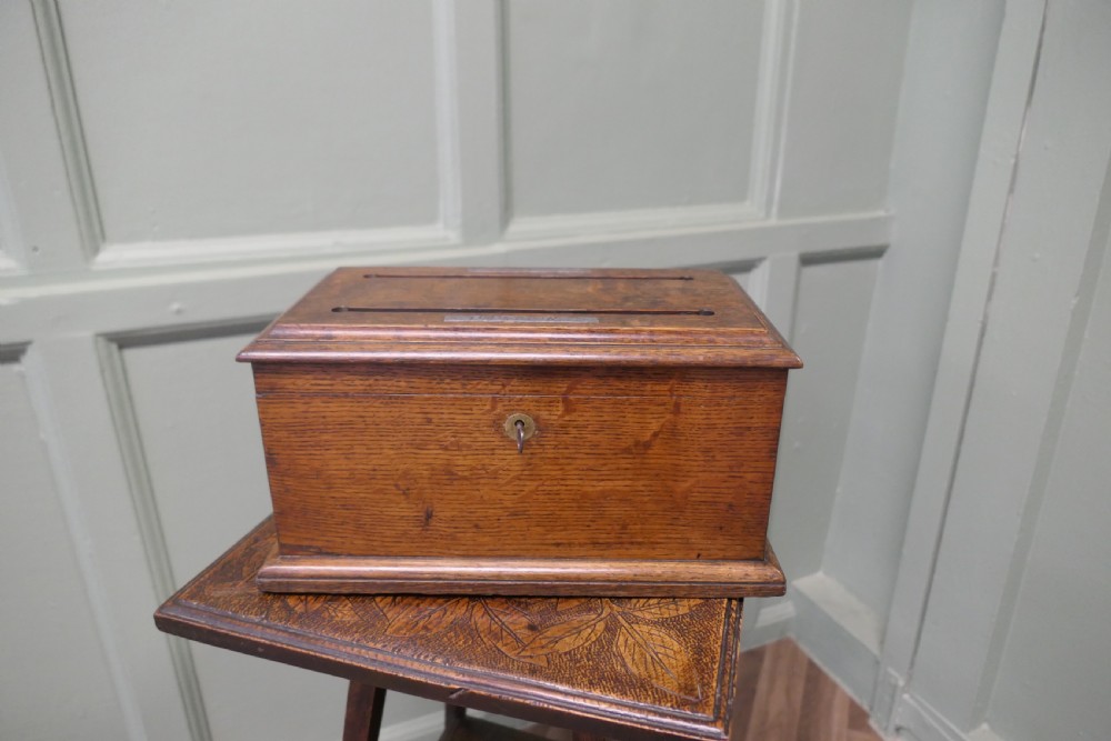 A rectangular golden oak correspondence letter box featuring top slots with metal plaques, a central brass keyhole escutcheon, and a moulded base.