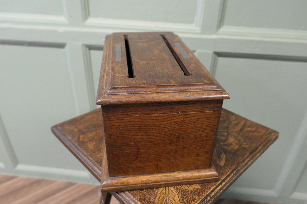 A rectangular golden oak correspondence letter box featuring top slots with metal plaques, a central brass keyhole escutcheon, and a moulded base. View VII