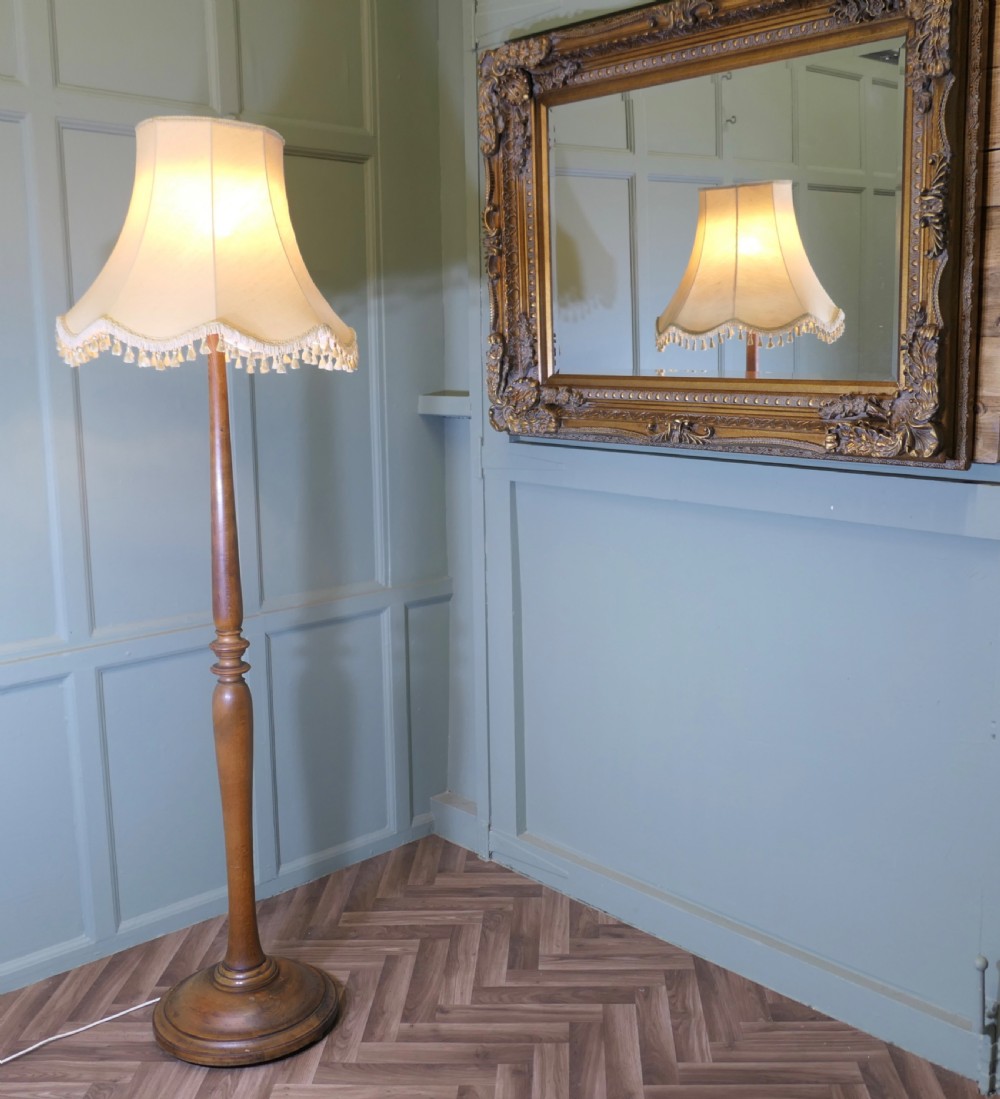 A tall turned beech standard lamp with a round moulded base and a cream fabric lampshade featuring tassel fringe. View II