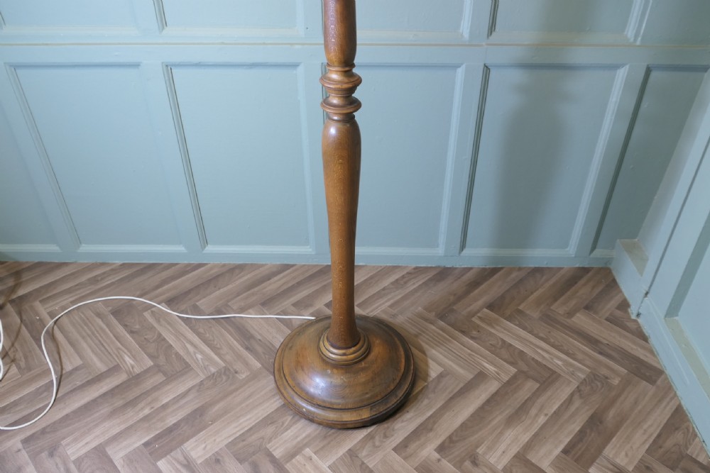 A tall turned beech standard lamp with a round moulded base and a cream fabric lampshade featuring tassel fringe. View V