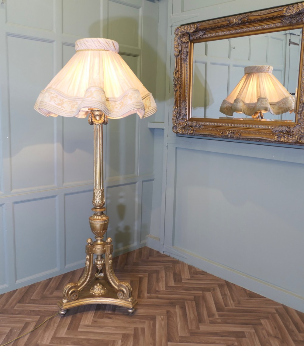 A tall antique carved giltwood floor lamp featuring a fluted column, scrolled tripod base, and a pleated cream fabric shade with embroidered trimming.