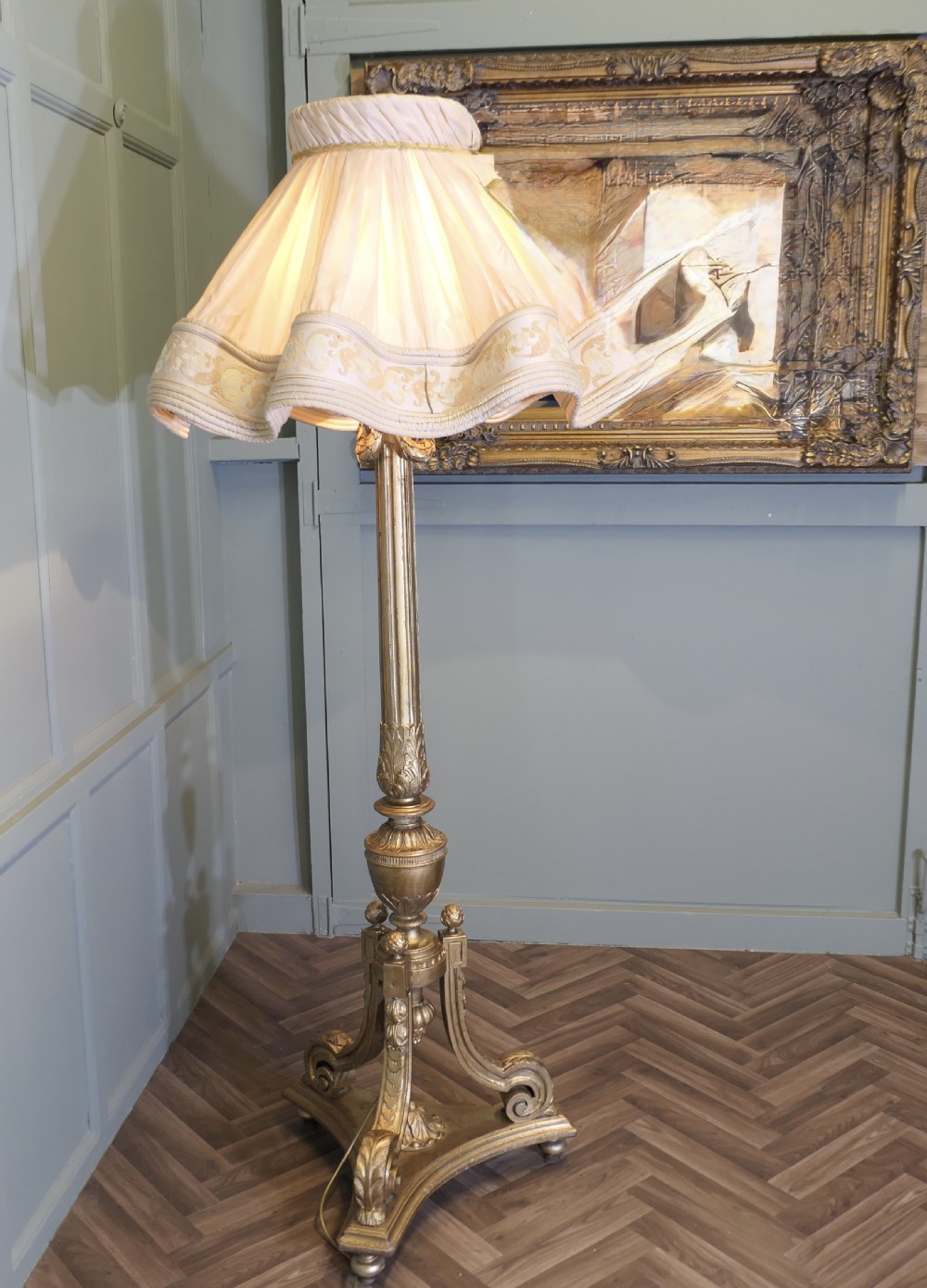 A tall antique carved giltwood floor lamp featuring a fluted column, scrolled tripod base, and a pleated cream fabric shade with embroidered trimming. View VI