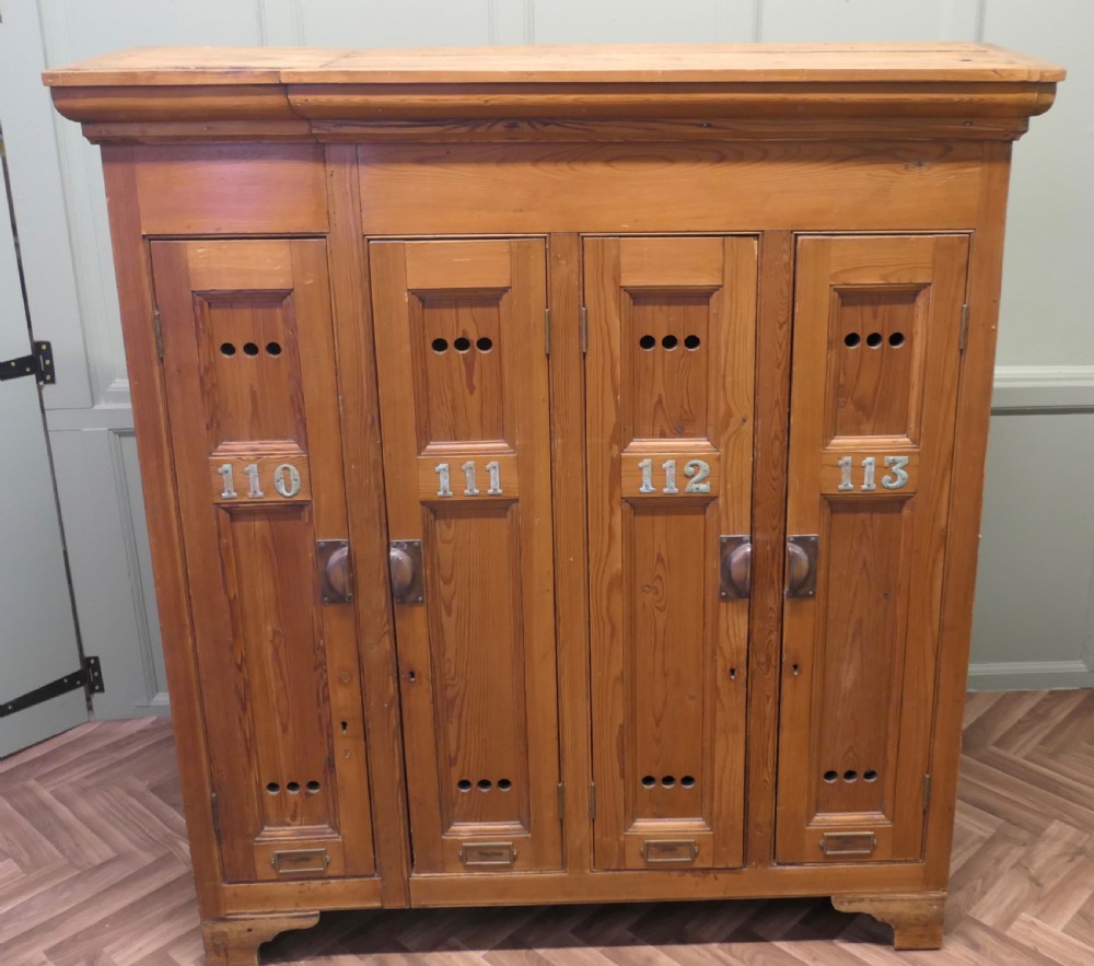 A four-door golden pine sports locker featuring numbered metal tags, circular ventilation holes, and brass fittings.