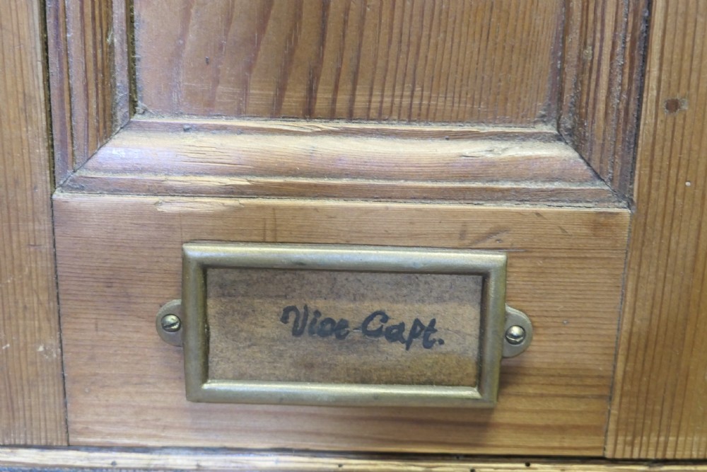 A four-door golden pine sports locker featuring numbered metal tags, circular ventilation holes, and brass fittings. View X