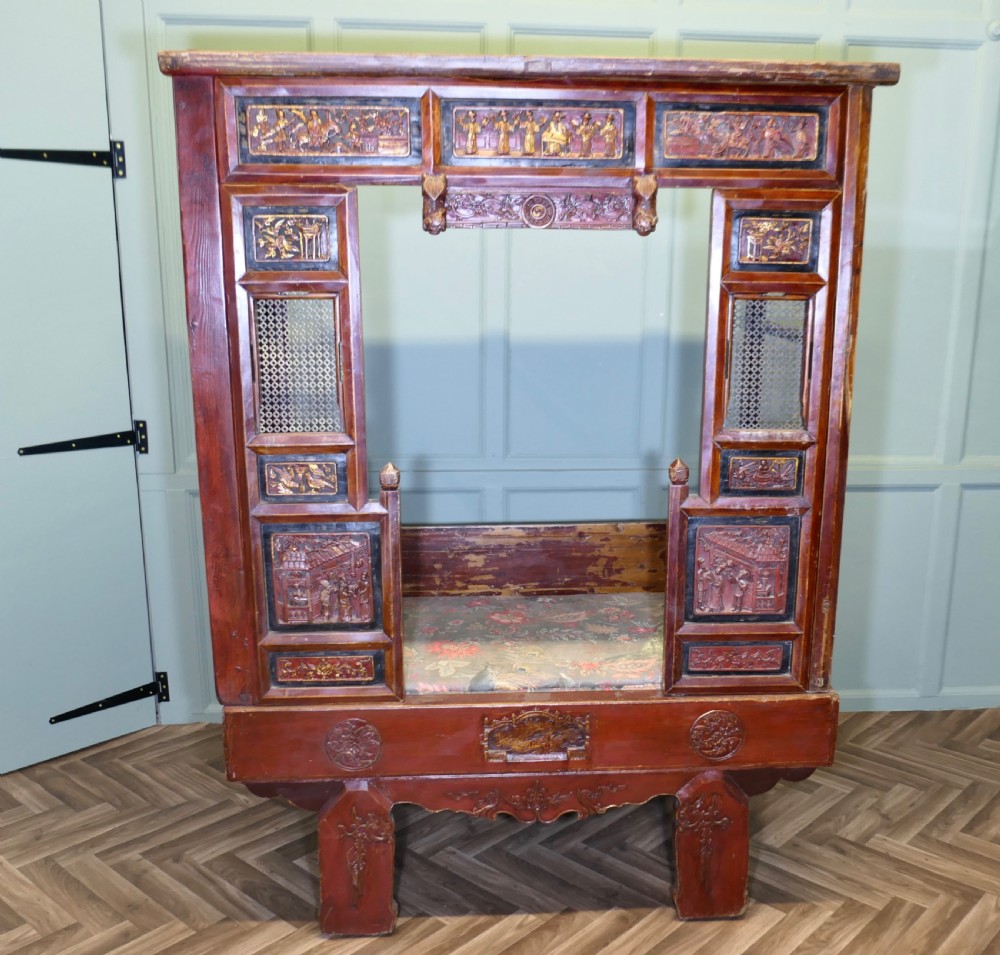 An antique Chinese red lacquered canopy bed decorated with carved gilded relief panels and lattice side screens.