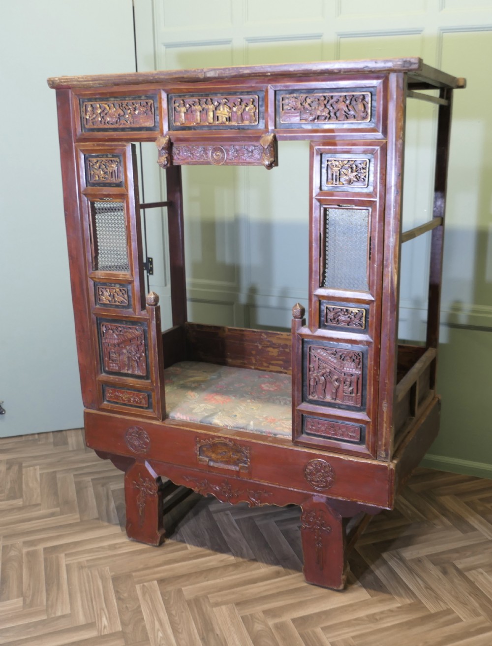 An antique Chinese red lacquered canopy bed decorated with carved gilded relief panels and lattice side screens. View II