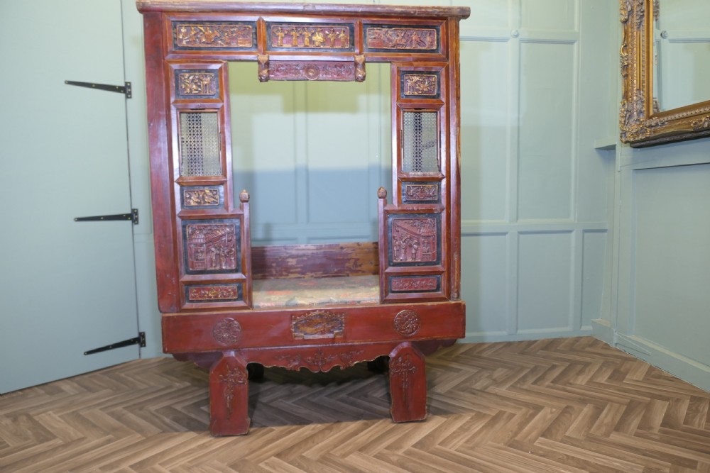 An antique Chinese red lacquered canopy bed decorated with carved gilded relief panels and lattice side screens. View VI