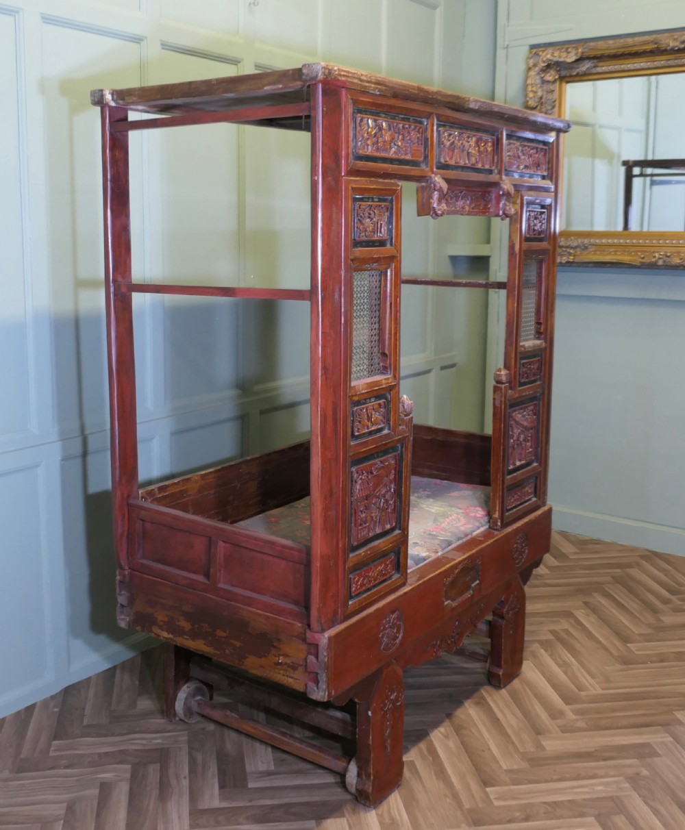 An antique Chinese red lacquered canopy bed decorated with carved gilded relief panels and lattice side screens. View VII