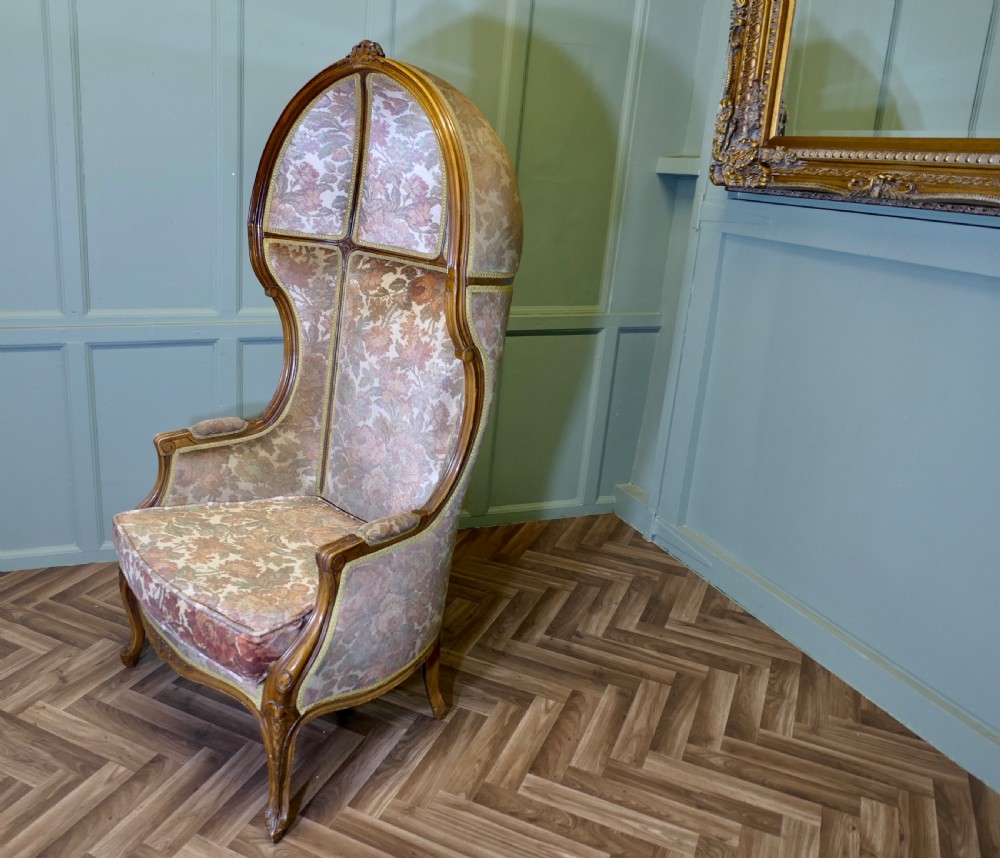 A French Rococo style hooded hall porter chair with a carved timber frame and patterned floral velvet fabric upholstery.
