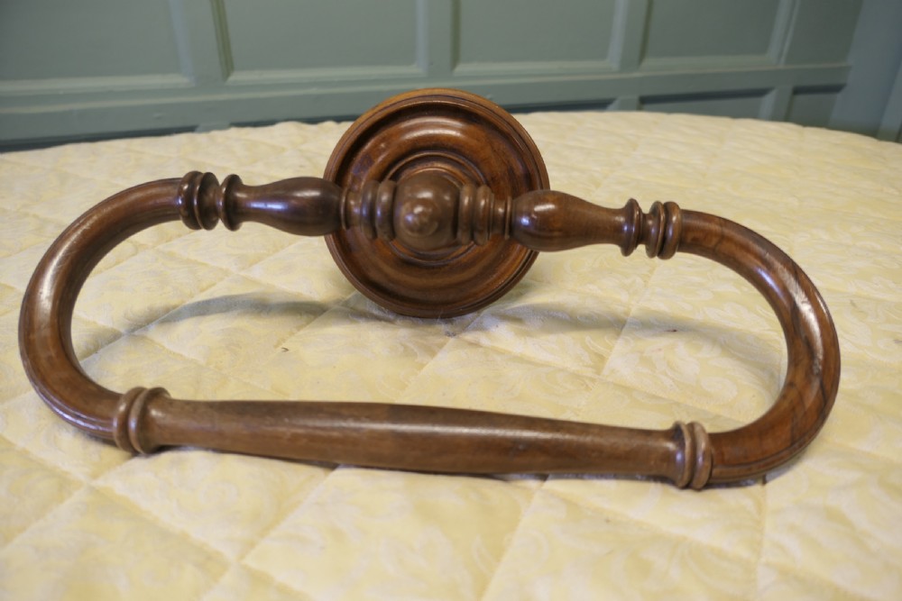 A turned walnut wall-mounted bed canopy frame with a circular backplate and curved drapery hoop.