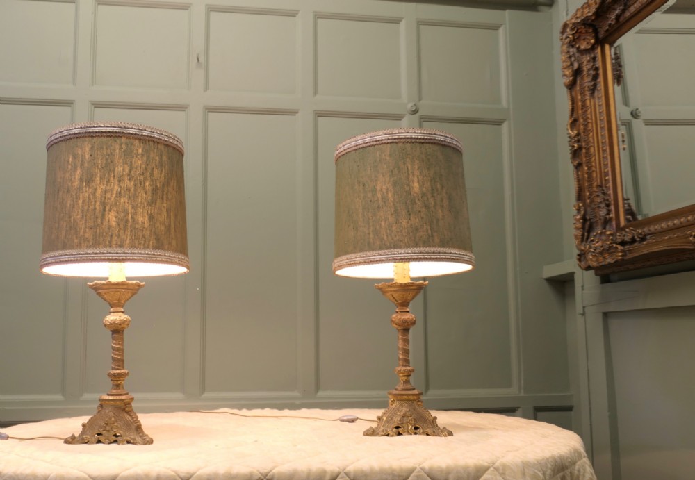 A pair of heavy French Gothic style brass table lamps featuring turned columns, ornate openwork bases, and green fabric shades.