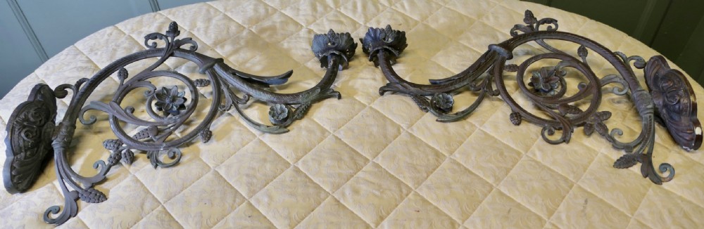A pair of elaborate dark patinated French bronze wall brackets featuring scrollwork, floral rosettes, and pinecone motifs.