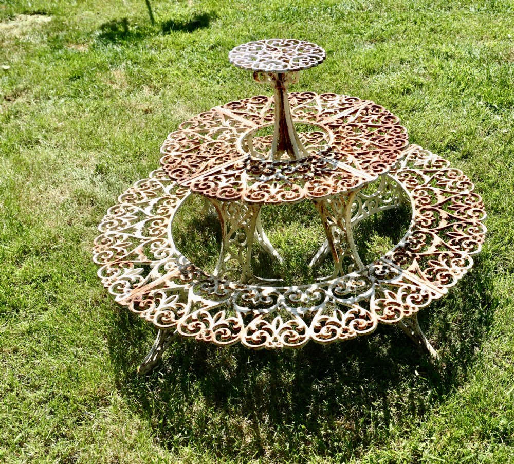 A circular three-tiered cast iron plant stand featuring intricate openwork scrollwork with weathered white paint and visible surface rust. View III